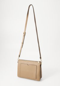 Koziana torba na ramię w kolorze tan, z teksturowanym wykończeniem, regulowanym paskiem, zapięciem na zamek i przednią kieszenią z subtelnym wycięciem.