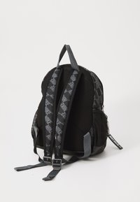 Crni ruksak sa sivim akcentima, podstavljenim trakama i mrežnim bočnim džepom. Ima uzorak s logotipom na trakama i oznaku "Samo uradi to".