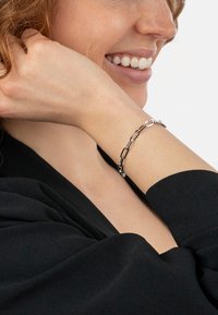 Silver chain bracelet featuring elongated links and a polished finish, worn on the wrist against a black fabric background.