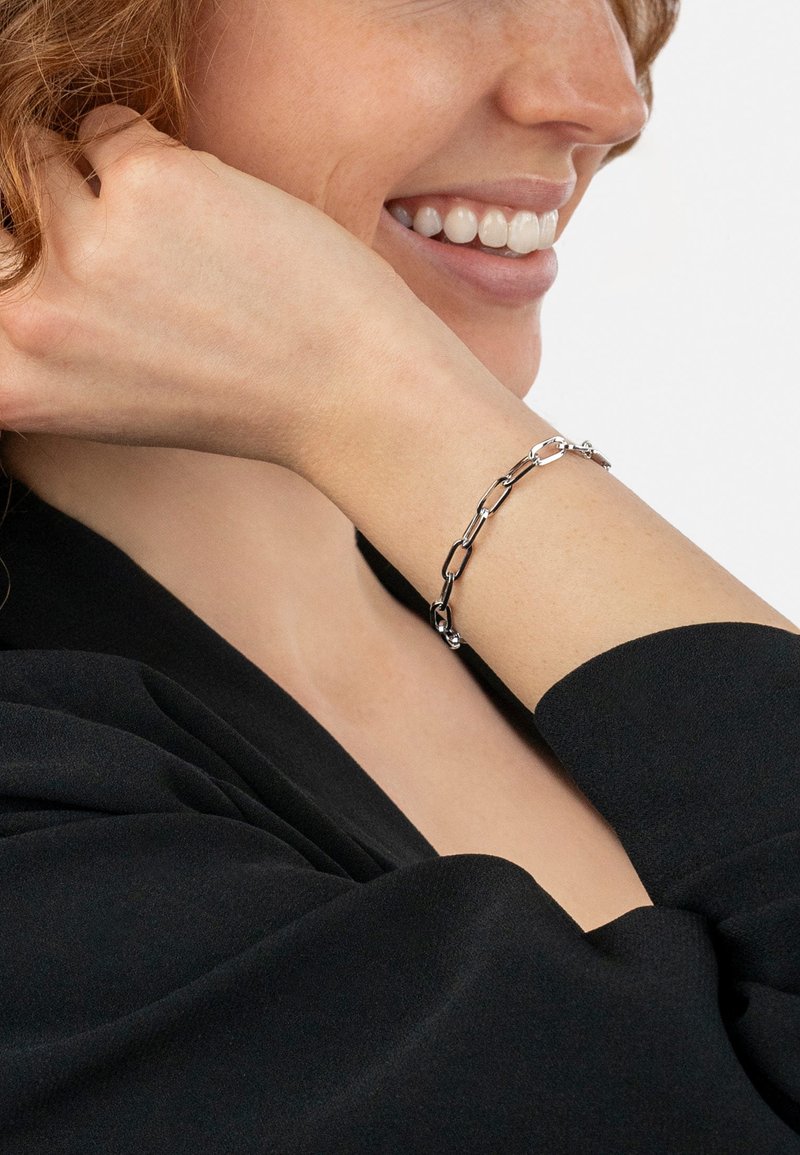 Silver chain bracelet featuring elongated links and a polished finish, worn on the wrist against a black fabric background.