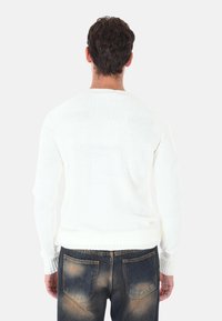 Maglione di colore bianco a maglia con scollo rotondo, polsini e orlo a coste, abbinato a jeans blu scuro con un leggero effetto usurato.