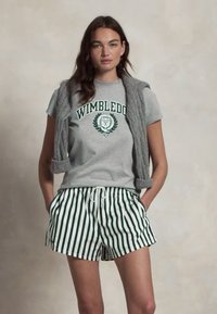 Pelēks īsām piedurknēm T-krekls ar uzrakstu "WIMBLEDON", zaļi un balti svītraini šorti, kā arī gaiši pelēks bezpiedurkņu teksturēts žakets.