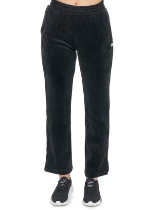 Modèle portant un pantalon noir en velours côtelé à jambes larges et à taille élastique, ainsi que des baskets noires, sur fond blanc.