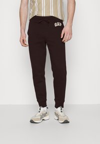 Bordeauxfarbene Jogginghosen mit gerippten Bündchen und elastischem Bund, versehen mit einem kontrastierenden, elfenbeinfarbenen "GAP"-Logo auf der linken Hüfte.