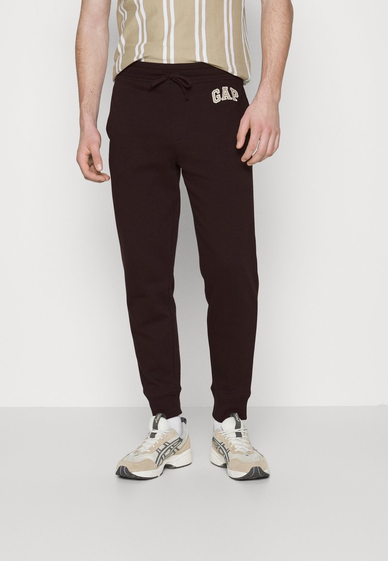 Bordeauxfarbene Jogginghosen mit gerippten Bündchen und elastischem Bund, versehen mit einem kontrastierenden, elfenbeinfarbenen "GAP"-Logo auf der linken Hüfte.
