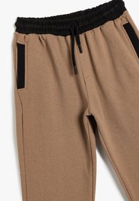 Beige sweatpants med en sort elastisk talje, snor og sidelommer. Blød tekstur med diskret stikning.