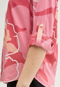Pink floral patterned shirt with rolled sleeves, featuring light and dark hues, single button detail on cuff, made from lightweight fabric.