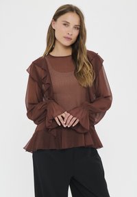 Brown sheer blouse with ruffled accents along the neckline and sleeves, featuring long, billowy sleeves and a flared hem.