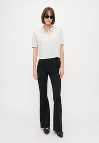 Crochet top s krátkým rukávem ve světle šedé barvě s límcem a button-up zapínáním, spárovaný s úzkými černými rozšířenými kalhotami a černými botami.
