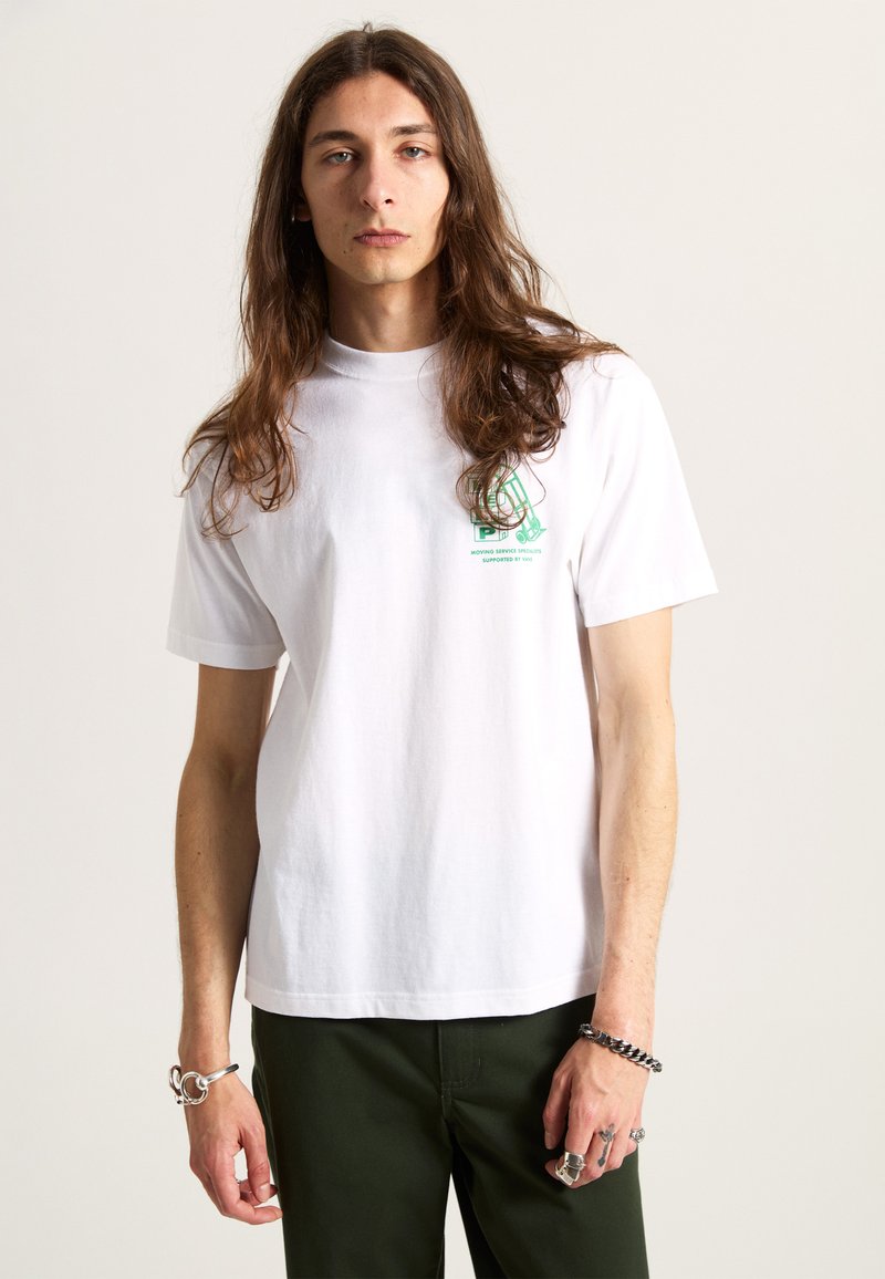 Vit bomull t-shirt med rund hals, korta ärmar och grön grafiktryck på vänster bröst. Tillsammans med mörkgröna byxor.