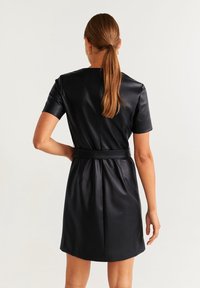 Robe noire en simili cuir avec des manches courtes, un corsage ajusté et une taille cintrée. Dotée d'une fermeture éclair à l'arrière et d'une texture lisse et élégante.