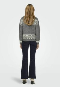 Pull en tricot gris avec des accents à motifs en blanc cassé, accompagné de pantalons évasés bleu foncé et de chaussures à talons carrés. Tissu texturé.