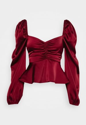 Tmavě červená saténová blůza s dlouhými rukávy, nařaseným výstřihem ve tvaru srdce, nadýchanými rameny, přiléhavým pasem a rozšířeným peplum lemem.