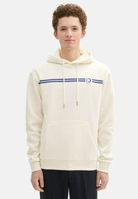 Sudadera color crema hecha de una tela suave, con un bolsillo frontal, cordón ajustable y dos franjas horizontales color azul marino en el pecho.