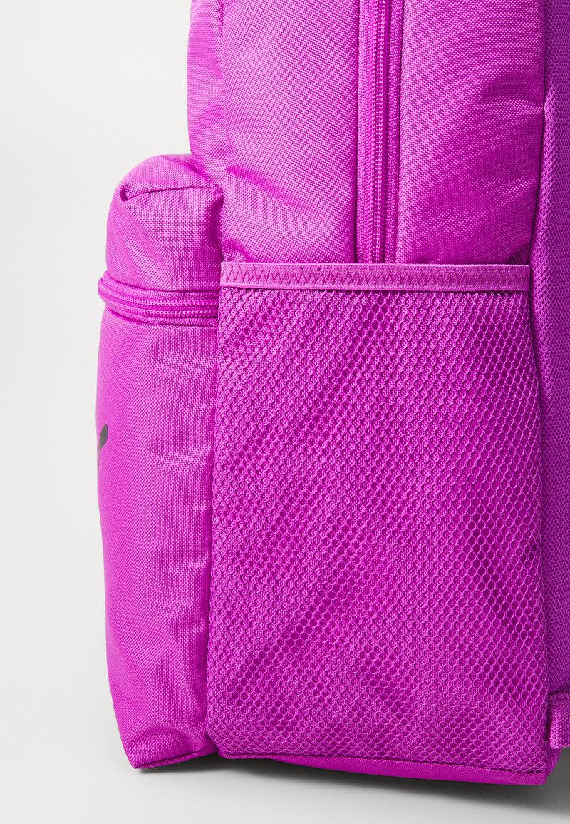 Sac à dos fuchsia avec une poche en maille texturée, un compartiment latéral lisse et une fermeture éclair bien en vue pour un accès facile. Construction en tissu durable.