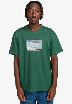 Grünes Baumwoll-T-Shirt mit grafischem Rechteck und dem Text "Grüße aus Barcelona". Rundhalsausschnitt, kurze Ärmel, lockere Passform.