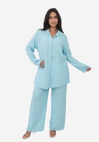 Jasnoniebieska, teksturowana, oversize koszula z guzikami, zestawiona z dopasowanymi szerokimi spodniami. Tkanina jest pomarszczona i lekka.