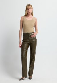 Beige geripptes Tanktop kombiniert mit dunkelgrünen, weiten Hosen aus Kunstleder. Schwarze Absatzschuhe runden das Outfit ab. Einfaches und modernes Design.