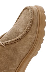 Chaussure en daim marron avec un bout rond, des coutures contrastées et une semelle texturée avec des rainures pour une meilleure traction. Fermeture à lacets plate.