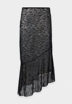 Femme debout portant une robe noire transparente sans manches à imprimé zèbre sur des sous-vêtements noirs et des bottines noires, devant un fond uni.
