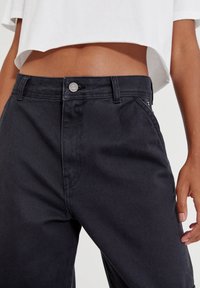 Musta farkut suoran leikkauksen kanssa, vyötäröllä metallinen nappi ja hienovarainen rakenne. Yhdistetty cropattu valkoinen toppi.