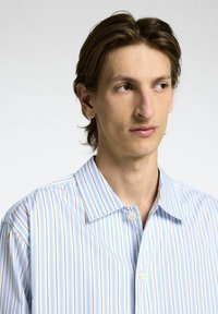 Knappskjorta med vertikala ränder i ljusblått, vitt och subtilt orange. Mjuk tygkvalitet med klassisk krage och lös passform.