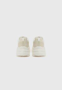 Bakside av beige og off-white sneakers med teksturert semsket skinn og mesh-overdel, tykk hvit midtsåle og kontrasterende hælkontakter.