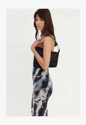 Zwarte gewatteerde schoudertas met een enkele strap en zilveren hardware, gecombineerd met een fitted, tie-dye patroon jurk in tinten zwart en crème.