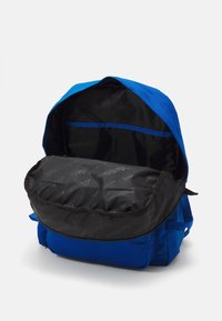 Modrý látkový batoh se zipem, který má černou podšívku se vzorem loga a samostatnou kapsu se zipem.