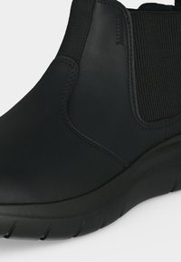 Κοντινή λήψη μαύρου μποτάκι slip-on με ελαστική πλαϊνή λεπτομέρεια και χοντρή σόλα, που δείχνει λείο δερμάτινο επάνω μέρος και ραμμένες λεπτομέρειες.