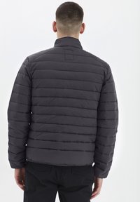 Giacca a piumino grigio scuro con motivo trapuntato orizzontale, collo alto e polsini elasticizzati. Caratterizzata da una chiusura con zip e materiale leggero.