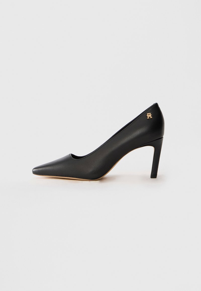 Black leather pointed-toe high heel shoe with mid-height stiletto heel and small gold emblem near heel on white background.
