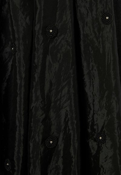 Tela negra con caída y un acabado texturizado, adornada con grandes acentos circulares de cuentas negras, cada una con un detalle de perla en el centro.