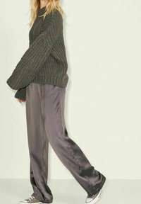 Chunky, dark green knit sweater paired with loose, metallic gray silk pants and low-top sneakers. Textured fabric and relaxed fit.