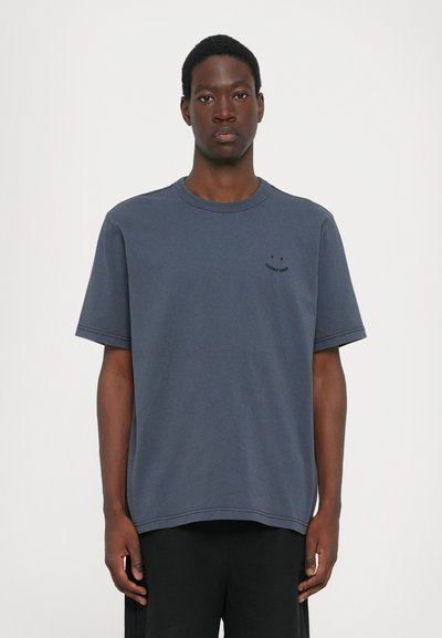 T-shirt en coton bleu marine avec un col rond, des manches courtes et un petit logo noir sur la poitrine. Coupe décontractée avec des détails de couture visibles.