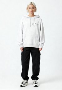 Felpa con cappuccio grigio chiaro con tasca frontale e scritta nera. Abbinata a pantaloni cargo neri con tasche laterali. Sneakers bianche con dettagli neri.