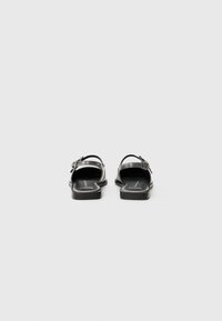 Black leather sandals with a flat sole and adjustable buckle. Minimalist design featuring an open back and smooth texture.