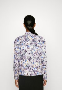Langærmet bluse med hvid baggrund og et blomsterprint i lilla, blå og gul. Glat stof med en klippet krave.