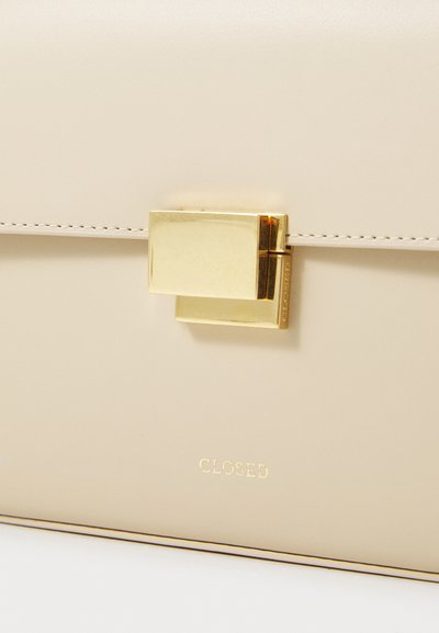 Beige nahkakäsilaukku, jossa on sileä pinta, kultasävyinen lukko ja kohokuvioitu "CLOSED"-logo edessä lähellä pohjaa.