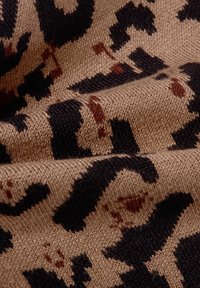  gestrickter Stoff in Beige mit einem Leopardenmuster in Schwarz und Braun. Die Textur wirkt weich mit sichtbaren Webdetails.