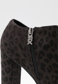 Černá semišová kotníková bota s leopardím vzorem, která má boční zip a masivní podpatek. Texturovaný povrch s hladkými akcenty.