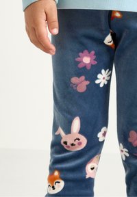 Pantaloni in pile di colore blu scuro con una varietà di facce di animali colorate e motivi floreali, con una consistenza morbida e una vita elasticizzata.
