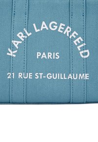 Tessuto azzurro chiaro con testo bianco in rilievo: "KARL LAGERFELD PARIS 21 RUE ST-GUILLAUME." Finitura liscia con dettagli cuciti.