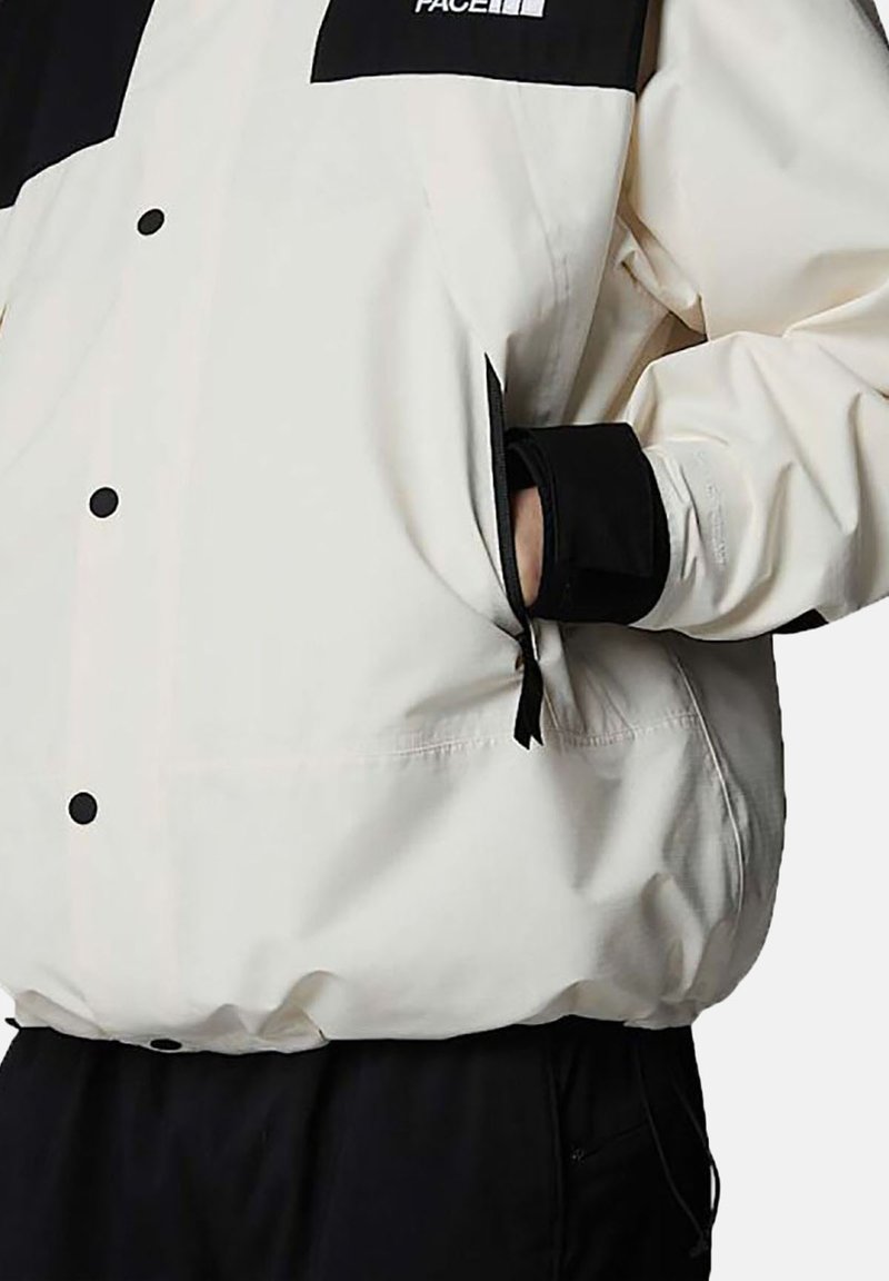 White lightweight jacket with black accents, snap buttons, and elastic cuffs. Features zippered pockets and a relaxed fit design.