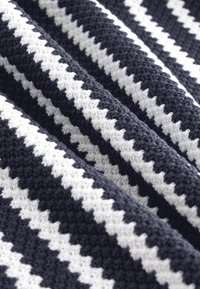 Strukturierte gewebte Decke in Marineblau und Weiß, mit einem Zickzackmuster aus wechselnden Farben und einer weichen, grobmaschigen Strickstruktur.