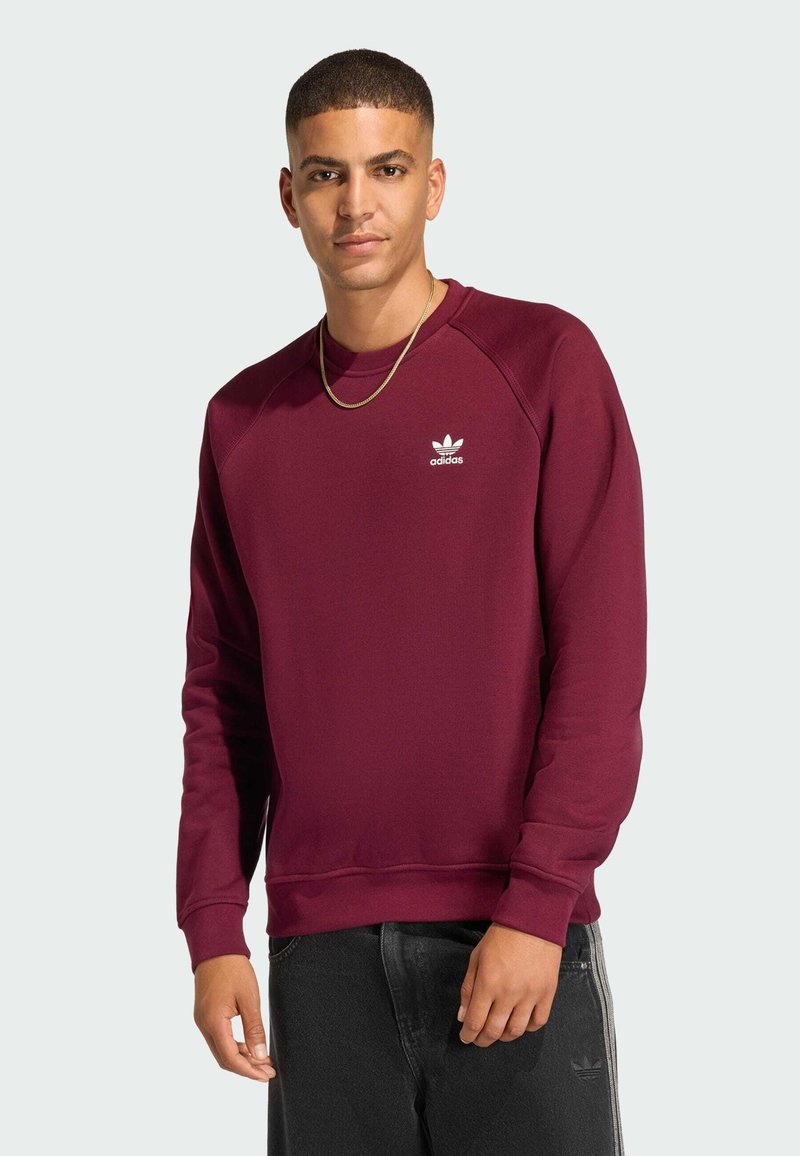 Burgundy sweatshirt made of cotton blend, featuring a ribbed crew neck and cuffs. White adidas logo on the chest. Black jeans with side stripes.