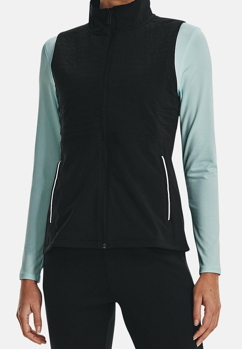 Gilet noir avec une partie avant matelassée, col montant et fermeture éclair. Chemise à manches longues bleu clair en dessous. Comprend des poches latérales avec des accents blancs.
