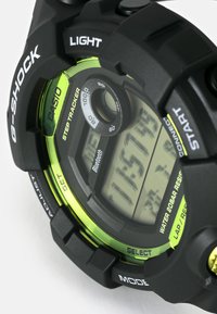 Schwarze digitale G-SHOCK-Uhr mit grünen Akzenten, ausgestattet mit einem Schrittzähler, wasserfest und einem großen LCD-Display mit seitlichen Tasten.