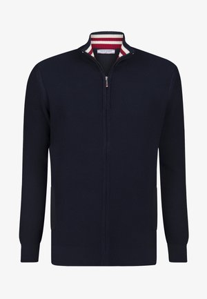 Navy zip-up sweater with ribbed texture, high collar, and striped inner collar in red and white. Features side pockets and fitted cuffs.