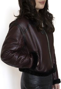 Bordeauxrode leren jas met ritssluiting, zwarte bontafwerking aan de kraag en manchetten, met een gestructureerd materiaal en een cropped ontwerp.